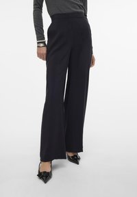Zwarte wijde broek gemaakt van textuurstof, met een hoge taille en strakke lijnen. Draag met puntige zwarte schoenen.