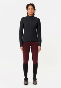 Μαύρο μακρυμάνικο σακάκι με ψηλό γιακά και πλήρες φερμουάρ, συνδυασμένο με εφαρμοστά μπορντό και μαύρα κολάν. Το σύνολο ολοκληρώνεται με αθλητικά παπούτσια.