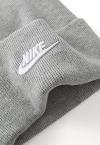 Gorro de malha cinza com textura canelada, apresentando o logótipo da Nike em branco bordado na bainha. O tecido parece suave e elástico.