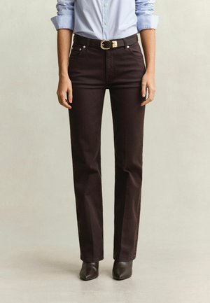 Personne portant un pantalon droit marron foncé, une ceinture noire à boucle dorée, une chemise bleu clair boutonnée et des bottes noires à bout pointu.