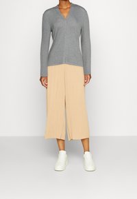 Grå v-ringad tröja i kombination med beige veckade culottbyxor, med långa ärmar och en avslappnad passform, kompletterad av vita sneakers.