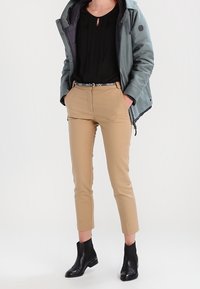 Khaki bukser med taperet pasform, sort top med plade, og en blågrøn parka. Sorte ankelstøvler og et mønstret bælte fuldender outfittet.