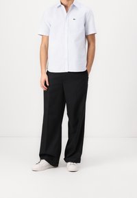 Vaaleansininen lyhythihainen paita, jossa pystysuora raidallinen kuvio ja rintatasku, yhdistetty mustiin leveälahkeisiin housuihin ja valkoisiin lenkkareihin.