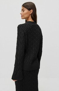 Svart stickad tröja med en texturerad kabeldesign, ribbad muddar och en avslappnad passform. Baksidan visar samma intrikata mönster.