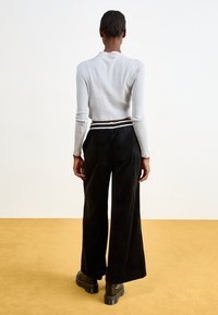 Fekete, bő szárú nadrág puha anyagból, csíkos derékpánttal díszítve. Világosszürke, bordázott, rövidujjú crop top-pal párosítva.