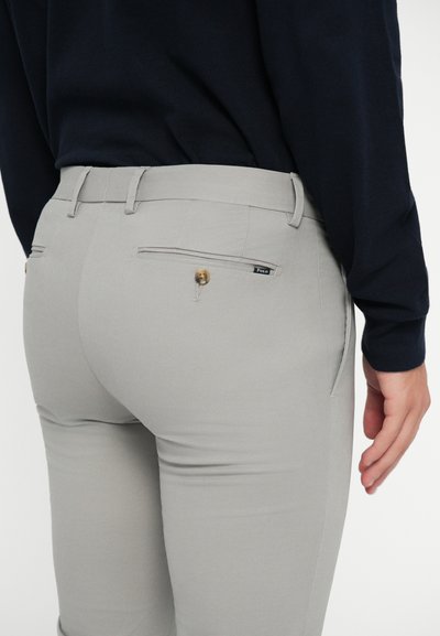 Pantalones gris claro de corte ajustado, con dos bolsillos traseros con cierres de botón y una etiqueta de marca sutil en el bolsillo derecho.