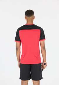 Miesten urheiluasu, jossa on punainen lyhythihainen paita mustilla yksityiskohdilla sekä mustat shortsit. Materiaali vaikuttaa kevyeltä ja hengittävältä.