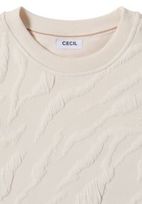 Pull créme, texturé par CECIL, présente un motif en relief et un col côtelé. Le tissu a une texture tricotée douce avec un design ondulé.