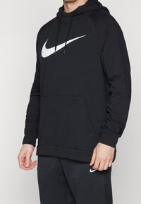 Sweat à capuche noir avec une poche avant, arborant un logo Nike blanc sur la poitrine et des poignets côtelés aux manches et à l'ourlet.