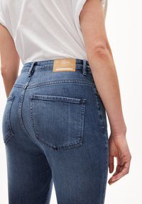 Jeans de mezclilla azul oscuro con una textura suave, que presentan una cintura alta, un diseño clásico de cinco bolsillos y un parche de cuero con marca en la parte posterior.