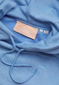 Blue hoodie made of soft fabric, featuring a drawstring hood, stitched logo "JJXX," and a fabric tag with size "S" and origin details.