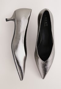 Fémes ezüstszínű, hegyes orrú magas sarkú cipő, texturált felülettel és vékony tűsarkúval. Fekete bélés és finom élkialakítás.