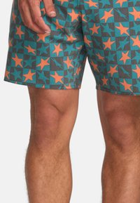 Costumi da bagno caratterizzati da un motivo a stelle teal e grigio con stelle arancioni, realizzati in materiale leggero, dotati di una cintura elastica e cuciture piatte.