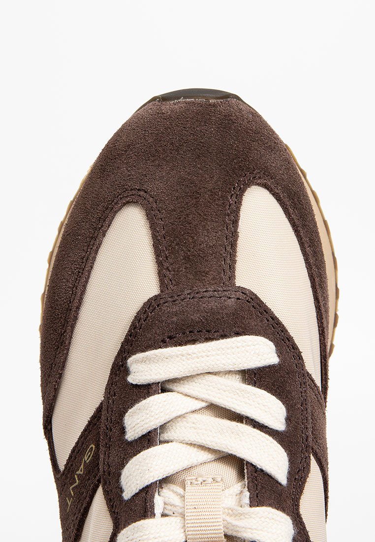 Braune Wildleder- und beigefarbene Stoffturnschuhe mit weißen Schnürsenkeln, runder Spitze und strukturiertem Zwischensohle. Goldene Markenprägung an der Seite.