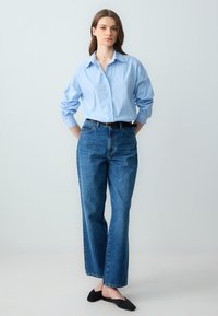 Blauw-wit gestreept overhemd met knopen, ontspannen pasvorm; gecombineerd met hoge, donkerblauwe denim jeans en zwarte platte schoenen, minimale accessoires.