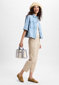 Lichtblauw denim overhemd met korte mouwen, beige tapered broek, tan loafers en een crème tote bag met blauwe accenten. Casual, ontspannen pasvorm.