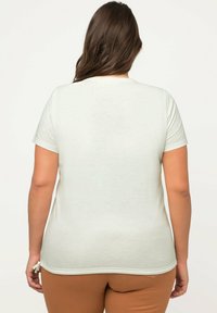 T-shirt verde chiaro a maniche corte con una vestibilità comoda, texture liscia e legature laterali all'orlo, mostrato di spalle.