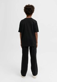 Czarny bawełniany t-shirt z krótkim rękawem i luźnym krojem, zestawiony z czarnymi spodniami w szerokim kroju i jasnymi trampkami.
