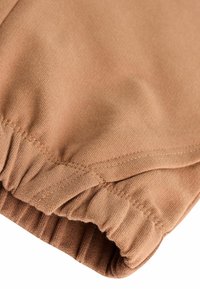 Tessuto stretching marrone con vita elasticizzata, caratterizzato da una texture liscia e cuciture piatte per un comfort aggiuntivo. Dettaglio del bordo arricciato visibile.