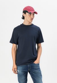 Marineblå bomulls T-skjorte med korte ermer og rund hals, kombinert med falmede blå jeans og en slitt rød caps.