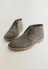 Botas de tobillo de ante gris con cierre de cordones, detalles de costura y suela de goma marrón contrastante. Textura suave; diseño de punta redonda.