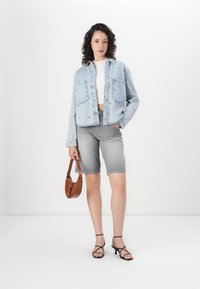 Denimjakke med blomsterbroderi, hvit crop top, grå bermudashorts, brun håndveske og svarte hælsandaler.