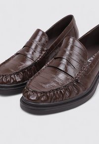 Brown leather loafers featuring a textured finish, decorative stitching, and gathered accents at the toe. Slip-on design with a low profile.