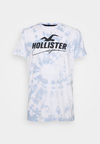 Bílý tričko s modrým tie-dye vzorem. Uprostřed hrudi je černé logo "Hollister California". Materiál je bavlna.