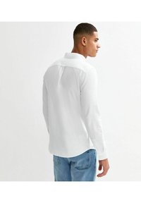 Witte lange mouwenshirt met een casual kraag en knoopmanchetten, met een rugplooi en een ronde zoom, gedragen met lichtblauwe jeans.