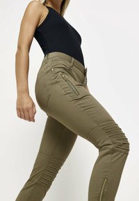 Olivgrön slim-fit byxor med siddragkedjor, ribbad textur och knäsyddetaljer. Matchas med en svart ärmlös topp.