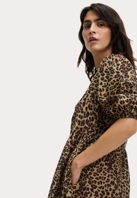 Robe en imprimé léopard de couleur beige et brune, avec des manches bouffantes et une taille froncée. Le matériau semble léger avec une finition texturée.