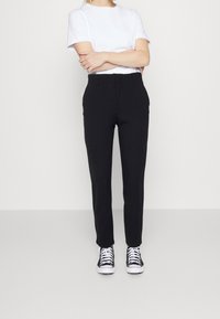 Pantalon noir ajusté avec une coupe droite, associé à un t-shirt blanc uni et des baskets montantes noires. Texture de tissu lisse.