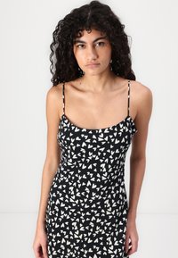 Rochie neagră cu model alb în formă de inimă, bretele subțiri și un design strâns. Materialul pare fin, cu un ușor luciu. Fără elemente hardware notabile.