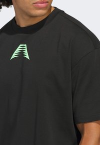 Czarna koszulka z krótkim rękawem wykonana z bawełny, z zielonym graficznym logo na piersi i okrągłym dekoltem. Gładka tekstura, luźny krój.