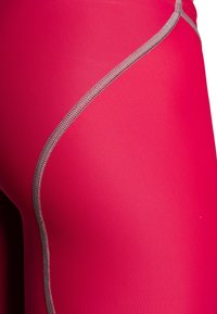 Gros plan sur un tissu extensible rose vif avec un détail de couture courbe grise prononcée.