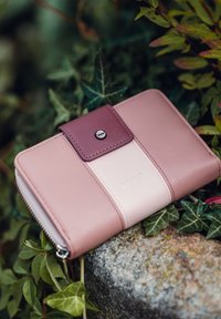 Leather wallet in pink and cream with a maroon snap closure, embossed logo, zipper detail, and a smooth, textured finish.