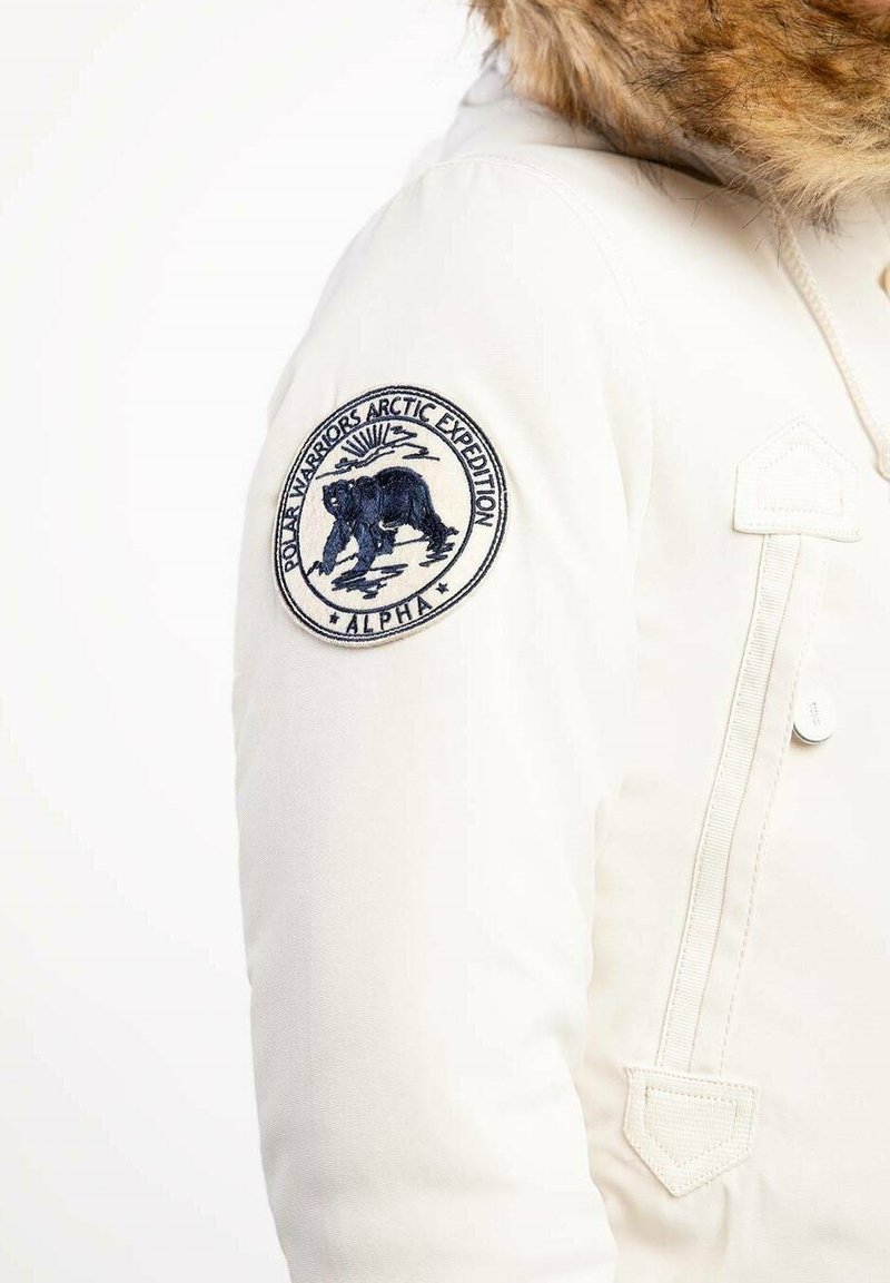 Weißer Parka mit Kapuze aus Fellbesatz, ausgestattet mit einem gestickten Patch mit einem Eisbären und dem Text "Polar Warriors Arctic Expedition".