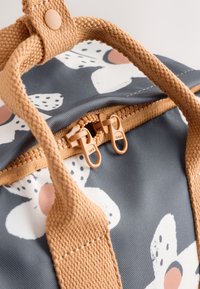 Small backpack with a gray floral pattern, beige textured straps, and dual zippers. Features a round button snap closure.