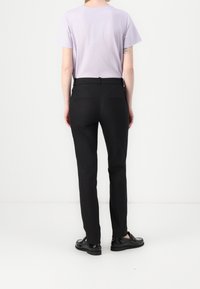 Pantalon noir cintré, avec une texture lisse, deux poches arrière et une ceinture plate, associé à une chemise violet clair.