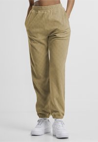Beige joggebukse med tekstur og diamantmønster, med sidelommer og elastisk midjebånd. Brukt med hvite sneakers.