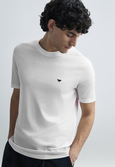 Weißes kurzärmeliges T-Shirt aus weicher Baumwolle, mit einem kleinen schwarzen Logo auf der Brust und einem Rundhalsausschnitt, mit entspannter Passform.