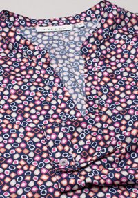 Blouse bleu marine avec un motif de formes géométriques colorées en rose, orange et blanc. Dotée d'un col droit et de poignets boutonnés.