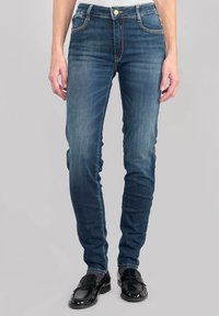 Jeans ajustados de denim azul oscuro con un leve desvanecimiento, diseño de cinco bolsillos y herrajes en tono dorado en la cinturilla. La textura es suave y ligeramente elástica.