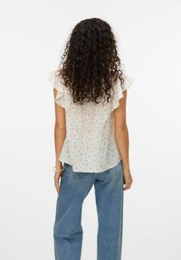 Hvid blomsterbluse med flæser på ærmerne, der har et delikat print af små lyserøde og grønne blomster, parret med løse blå denim jeans.