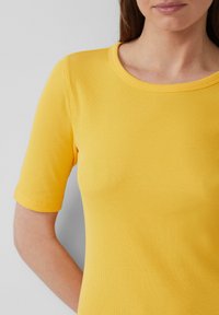 Haut jaune à manches courtes avec un col rond. La texture est légèrement reliefée, mettant en valeur l'élasticité et la coupe du tissu.