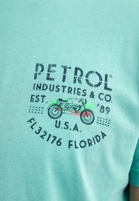 Tyrkysové bavlněné tričko s potiskem motocyklu v černé a zelené barvě, s textem "PETROL INDUSTRIES & CO. EST. '89 U.S.A."
