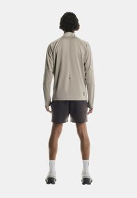 Šviesiai pilkas ilgomis rankovėmis palaidinė su aukštu apykakle, derinama su tamsiomis šortais. Minkšta medžiaga, minimalūs siūlės ir mažas logotipas ant apatinio krašto.