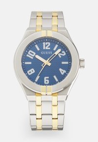 Orologio in acciaio inossidabile con quadrante blu testurizzato, audaci indici ore bianchi e bracciale in argento con accenti dorati. Presenta una corona sul lato.