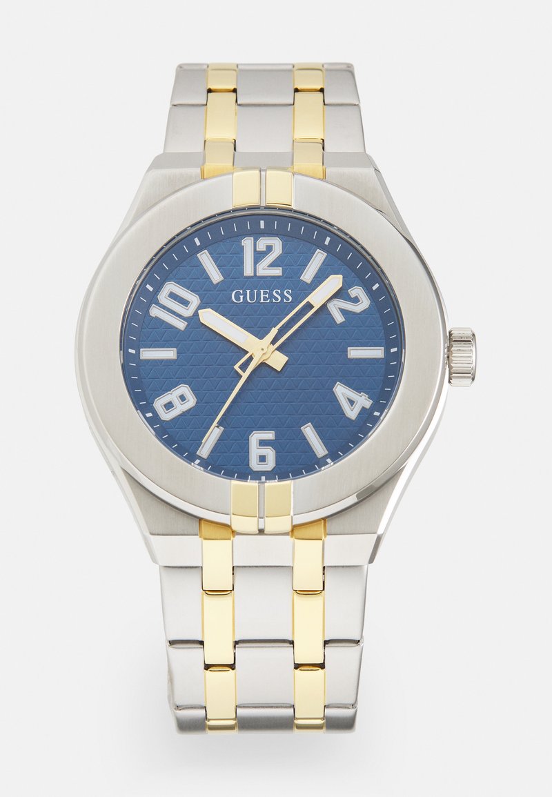 Montre en acier inoxydable avec un cadran texturé bleu, de grands index blancs, et un bracelet argenté avec des accents dorés. Présente une couronne sur le côté.