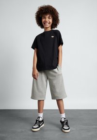 Svart bomullströja med korta ärmar, grå knälånga shorts i jersey-tyg och svart-vita sneakers med ränder.
